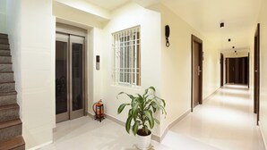 A hallway with a potted plant, a fire extinguisher, and an elevator. - Greens Venue (Chennai)