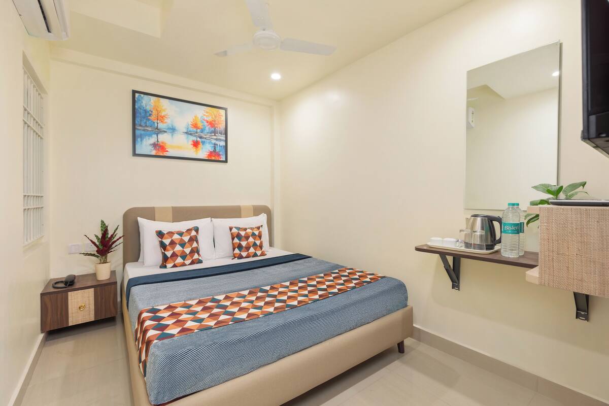 A bedroom with a bed, a nightstand, a wall-mounted shelf with a mirror, a painting, and a ceiling fan.