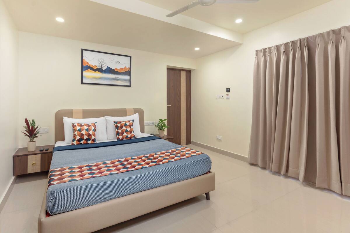 A bedroom with a bed, a ceiling fan, a painting, a door, and a window with curtains.