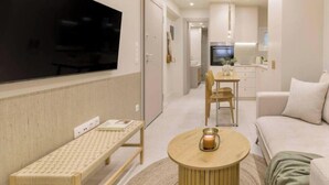 Ett modernt vardagsrum med en platt-TV, ett runt soffbord, en soffa och en matplats med ett bord och stolar.