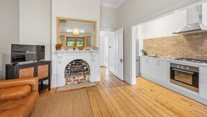A modern kitchen with a brick fireplace, white cabinetry, and a television in the living area. - Apartment Faro - Heart of South Freo with Parking (South Fremantle)
