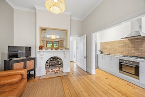 A modern kitchen with a brick fireplace, white cabinetry, and a television in the living area. - Apartment Faro - Heart of South Freo with Parking (South Fremantle)
