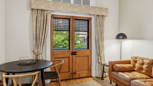 A room with a wooden door, a round table with a chair, a leather sofa, and a floor lamp. - Apartment Faro - Heart of South Freo with Parking (South Fremantle)