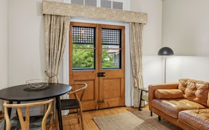 A room with a wooden door, a round table with a chair, a leather sofa, and a floor lamp. - Apartment Faro - Heart of South Freo with Parking (South Fremantle)