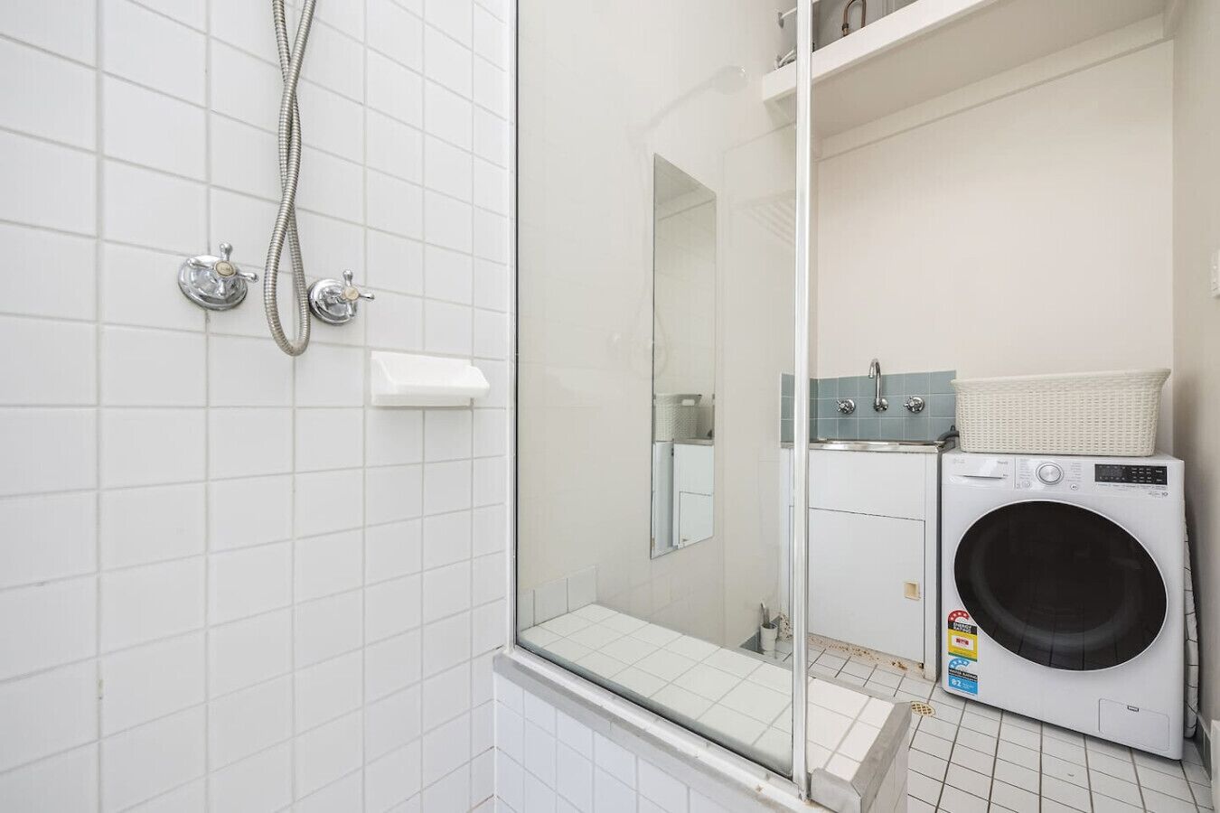 A bathroom with a shower, a mirror, a sink, and a washing machine.