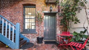 A brick building with a grey door, a window with bars, a blue staircase, and red outdoor furniture. - Apartment Faro - Heart of South Freo with Parking (South Fremantle)