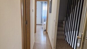 A corridor with a wooden door on the left, a white wall, and a staircase with black railings on the right. - Apartment 'Elisa' with Wi-Fi and Air Conditioning (Moraira)