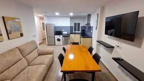 A living room with a sofa, a wooden dining table, and chairs, a kitchen with appliances, and a TV mounted on the wall. - Apartment 'Elisa' with Wi-Fi and Air Conditioning (Moraira)