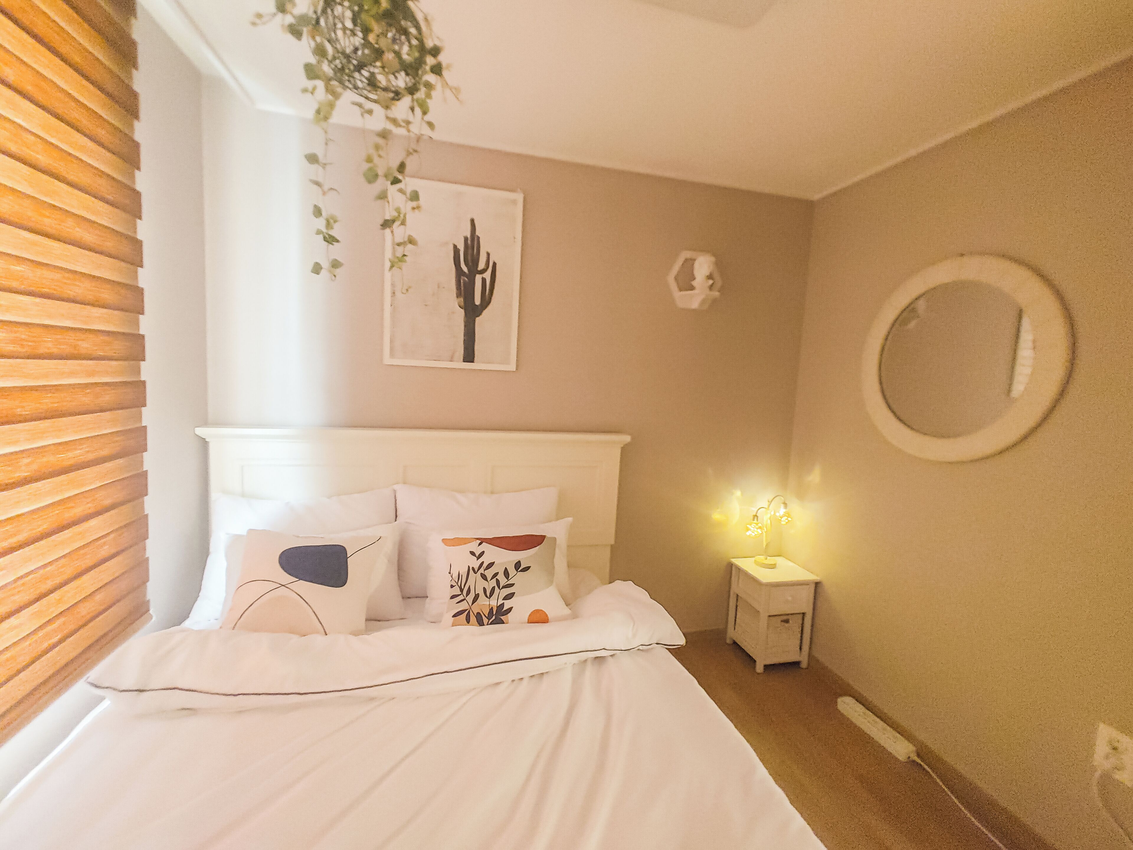Une chambre à coucher avec un lit, une table de chevet, des œuvres d’art murales et une plante suspendue.