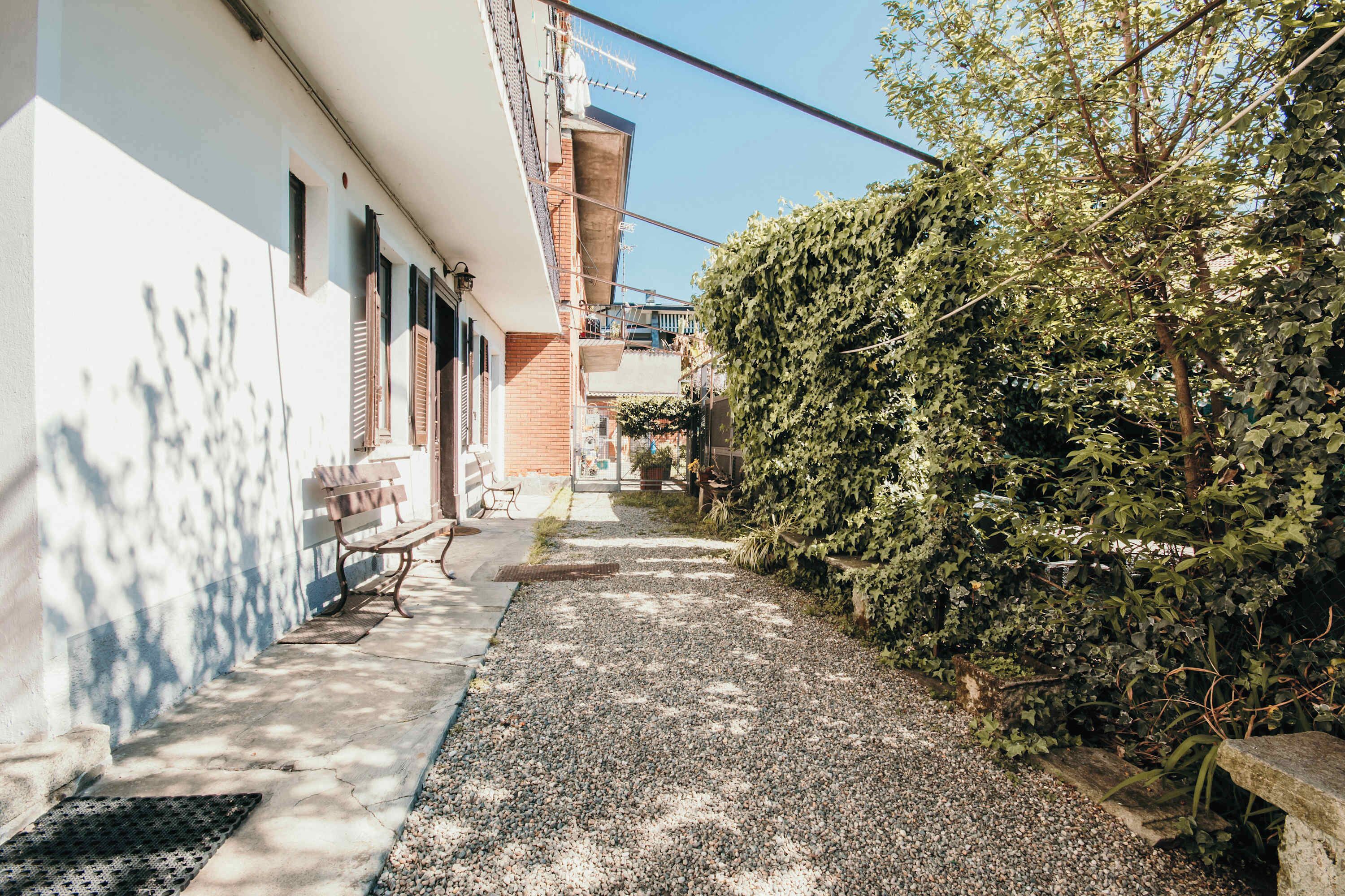 Une ruelle étroite avec un banc, une haie et un immeuble doté d’un balcon.