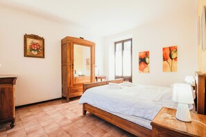 A bedroom with a bed, wooden wardrobe, bedside table, lamp, and artwork on the wall. - La casa di Solcio  - Lakeside L&B (Lesa)