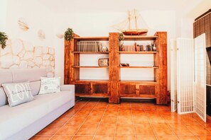 Ein Wohnzimmer mit einem weißen Sofa, einem Holzregal und einem Fliesenboden.