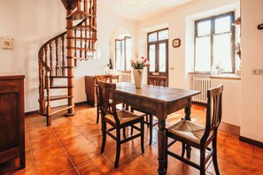 A dining area with a wooden table and chairs, a spiral staircase, and large windows. - La casa di Solcio  - Lakeside L&B (Lesa)
