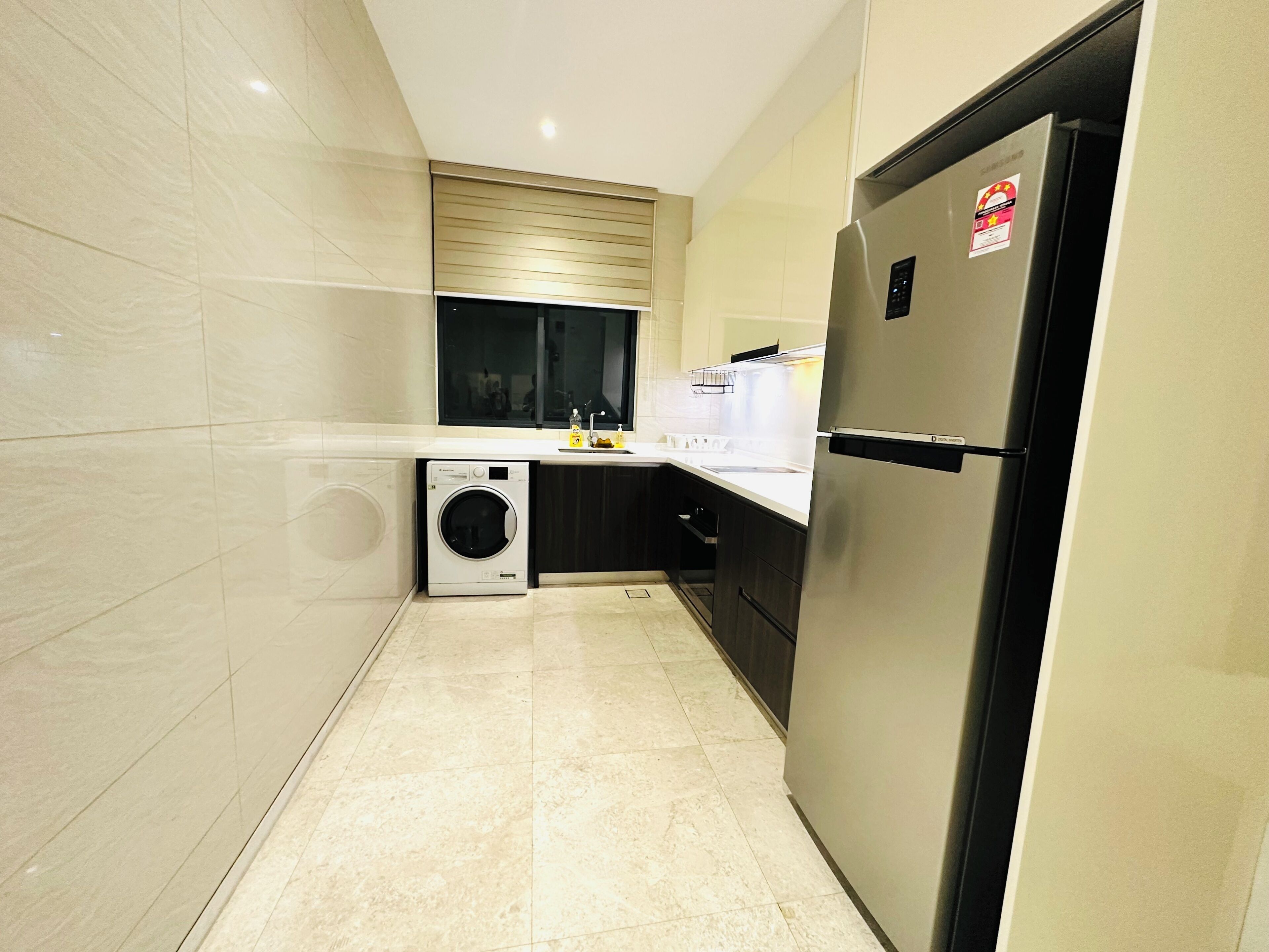 A modern kitchen with a built-in washing machine, a stainless steel refrigerator, and a window above the sink.