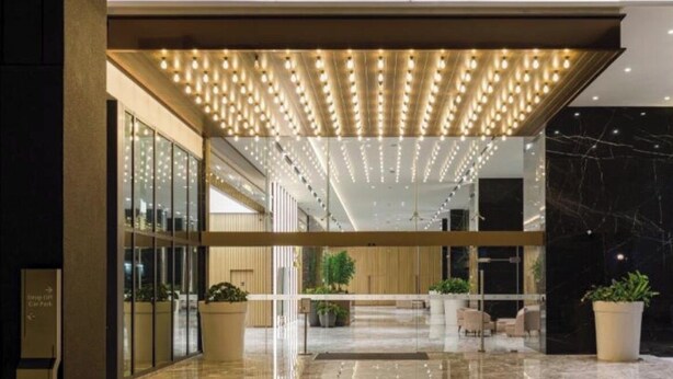 Un hall d’entrée moderne avec un sol réfléchissant, des murs en verre et un plafond agrémenté d’un luminaire décoratif.