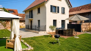Uma casa de dois andares com varanda, um pátio com móveis de exterior e churrasqueira.