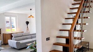 Um interior moderno com escada de madeira, sofá cinza e luminária pendente.