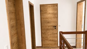 Um corredor com piso de madeira, uma porta de madeira e uma escada com guarda-corrimão de vidro.