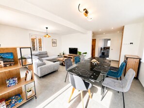 Een moderne woonkamer met een eettafel, banken, een televisie en een keukenhoek.