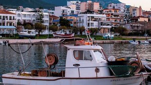 Un pueblo costero con barcos amarrados cerca de un puerto deportivo, edificios al fondo y un paisaje montañoso.