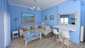 Una sala de estar con un sofá, una mesa de comedor y dos sillas. Hay un cuadro en la pared y un espejo con un marco decorativo.