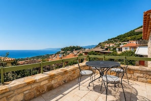 Eine Terrasse mit Steinmauern, einem runden Tisch und Stühlen mit Blick auf ein Küstendorf.