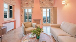 A cozy living room with a stone fireplace, two sofas, a coffee table with a vase, and a view through the glass doors. - Kyparissia Aries Stone Maisonette, Panoramic Views (Kiparissia)