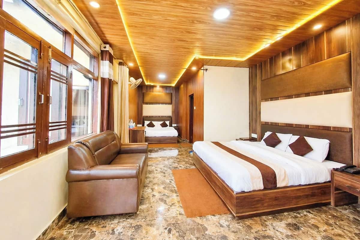 Quarto de hotel com uma cama grande, um sofá, teto de madeira e janelas amplas.