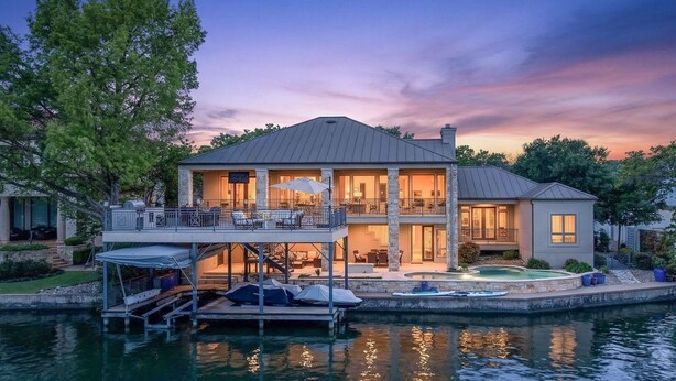 Una casa frente al agua con muelle, mobiliario exterior y piscina.