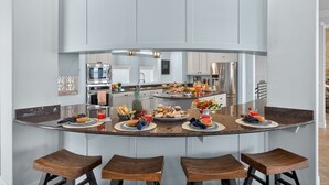 Una cocina moderna con una isla curva, taburetes de bar y una isla central con comida y bebidas.