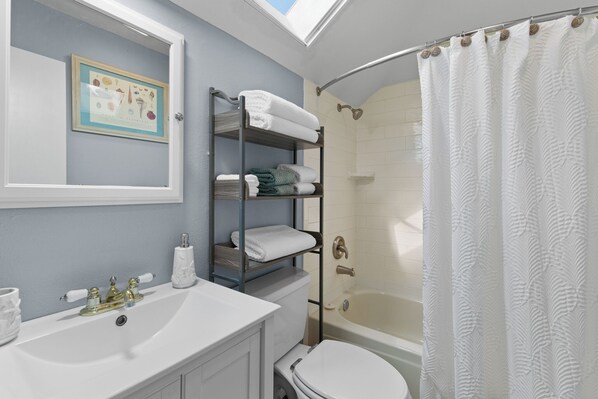 A bathroom with a shower, a sink, a toilet, a towel rack, and a framed picture on the wall.