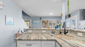 A kitchen with a marble countertop, white cabinets, a sink, and a staircase leading to another level. -  Welcome to Cocktails & Dreams! A Serene Waterfront Retreat w/ Direct Bay Access (Port Isabel)