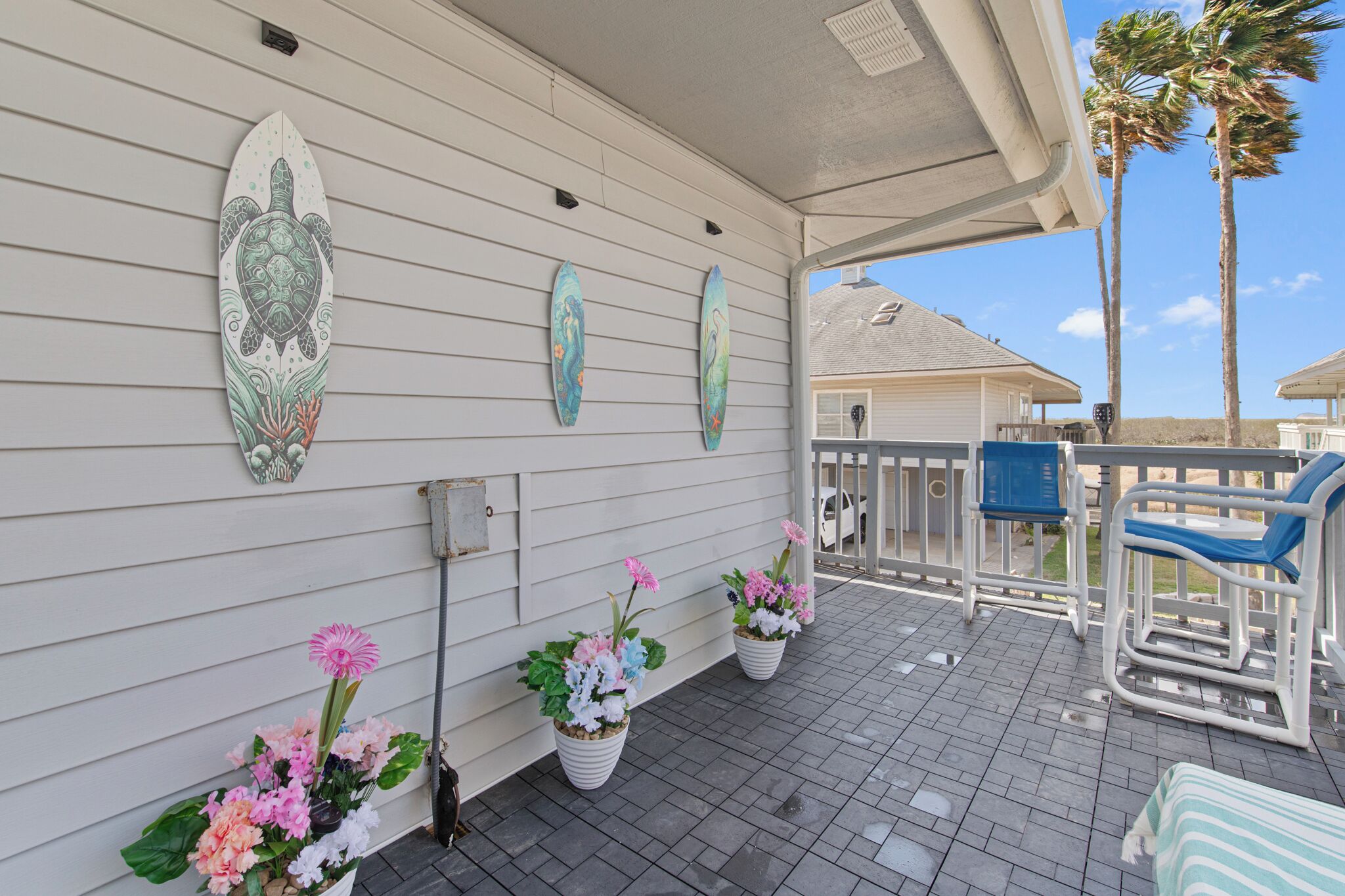 Une terrasse couverte agrémentée de planches de surf, de plantes en pot et de mobilier d’extérieur.