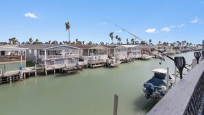 A waterfront property with multiple docked boats, a clear sky, and a row of houses along the water. -  Welcome to Cocktails & Dreams! A Serene Waterfront Retreat w/ Direct Bay Access (Port Isabel)