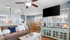 A living room with a brown leather sofa, a white coffee table, a dining area with wooden chairs, and a green cabinet with glass doors. -  Welcome to Cocktails & Dreams! A Serene Waterfront Retreat w/ Direct Bay Access (Port Isabel)