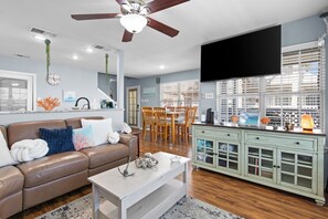 A living room with a brown leather sofa, a white coffee table, a dining area with wooden chairs, and a green cabinet with glass doors.