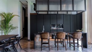 Une cuisine moderne avec des meubles de couleur sombre, un îlot central doté de tabourets et une plante en pot.