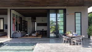 Un espace de vie extérieur moderne, doté d’une piscine, d’une table à manger et de chaises, et attenant à un patio couvert.
