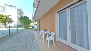 Een balkon met een betegelde vloer, een bakstenen muur, een schuifdeur en een kleine tafel met stoelen.