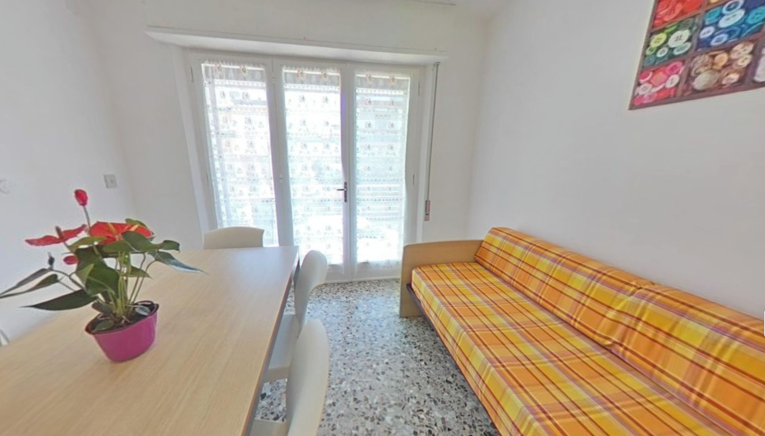 Ein Zimmer mit einer Couch, einem Tisch, einer Topfpflanze und einem Fenster mit Jalousien.