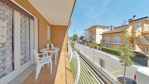 A balcony with a table and chairs, a view of a street with buildings, and a clear sky. - Enchanting Villa in a Peaceful Area (Lignano Sabbiadoro)
