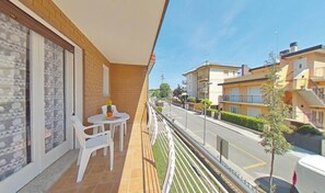 Ein Balkon mit Tisch und Stühlen, Blick auf eine Straße mit Gebäuden und einem klaren Himmel.