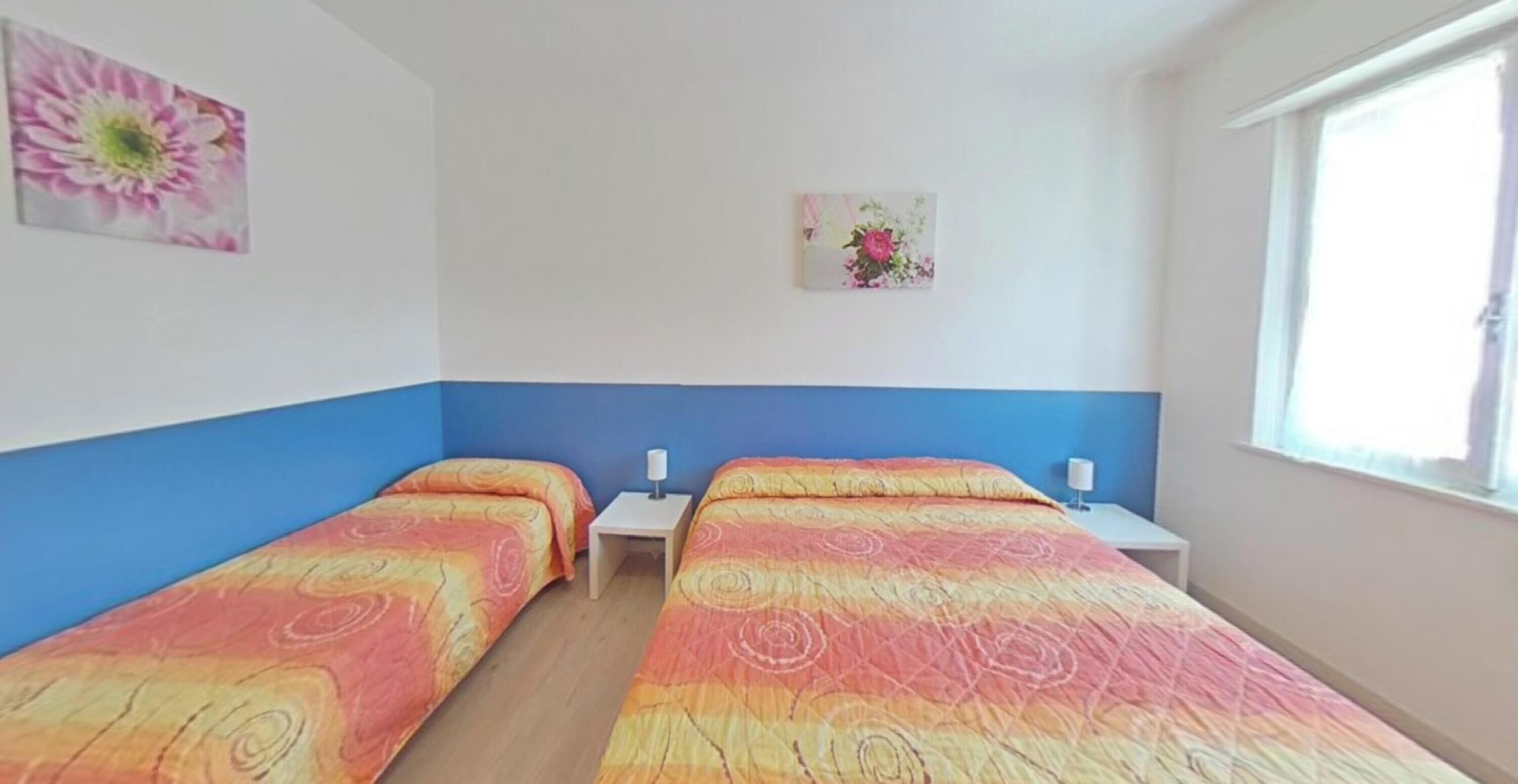 Een kamer met twee bedden, een raam en twee wandlampen.
