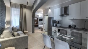 A modern kitchen with stainless steel appliances, a dining area with a glass table, and a living area with a sofa and curtains. - LF Borgo Trastevere (Rome)