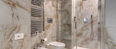 A bathroom with a marble wall, a glass shower enclosure, a bidet, and a toilet.