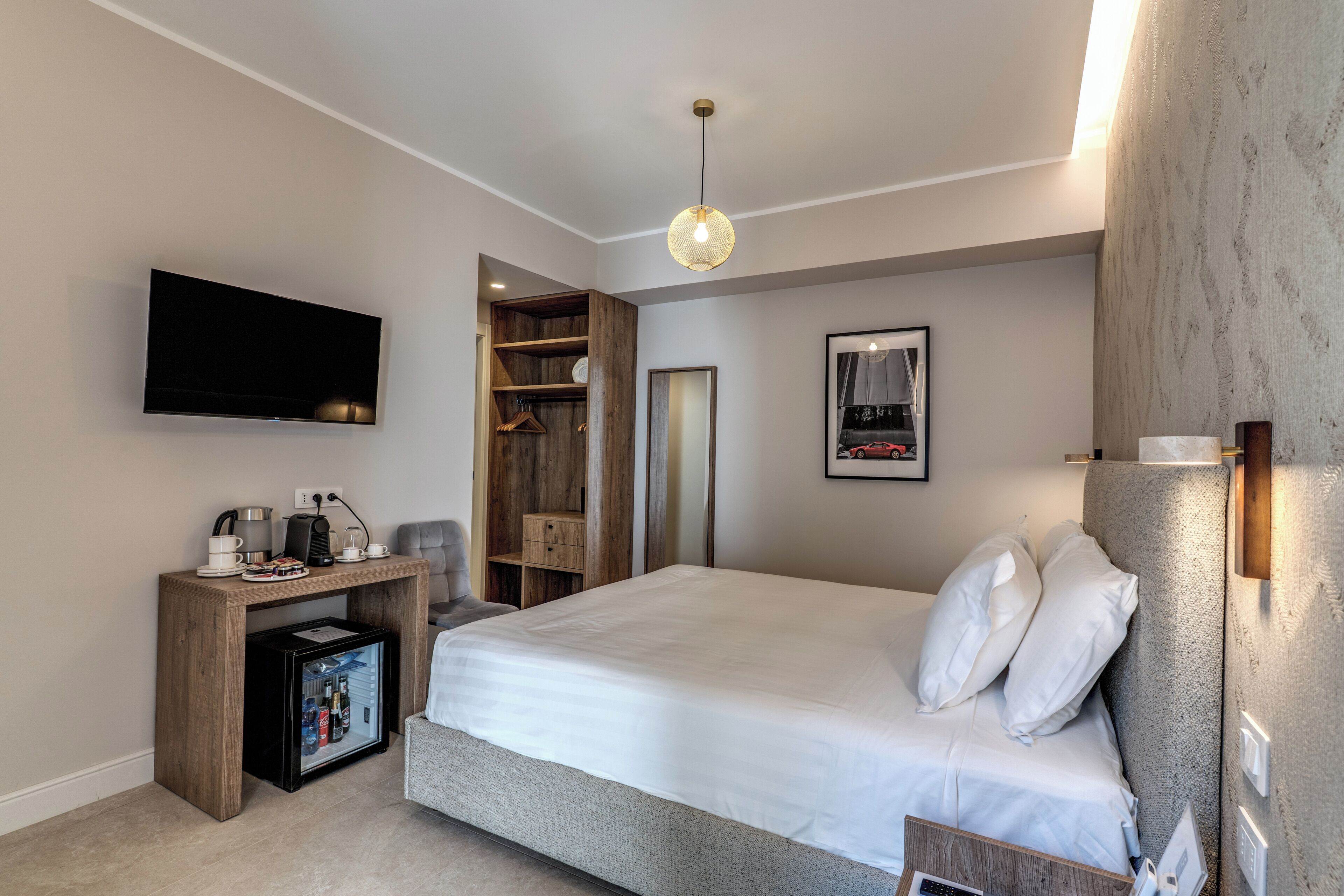 Une chambre d’hôtel équipée d’un lit, d’une télévision, d’un mini-bar, d’un bureau en bois et d’une armoire.