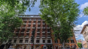 A multi-story building with balconies, storefronts, and parked cars. - LF Borgo Trastevere (Rome)