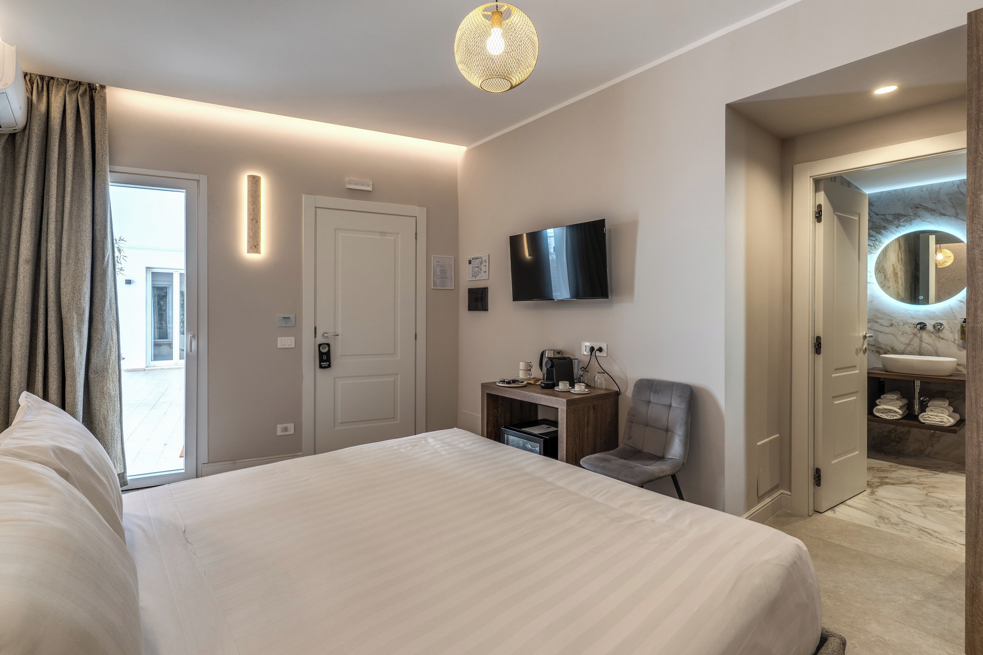 Habitación de hotel con una cama grande, televisor, escritorio con silla, baño con lavamanos de mármol y espejo circular.