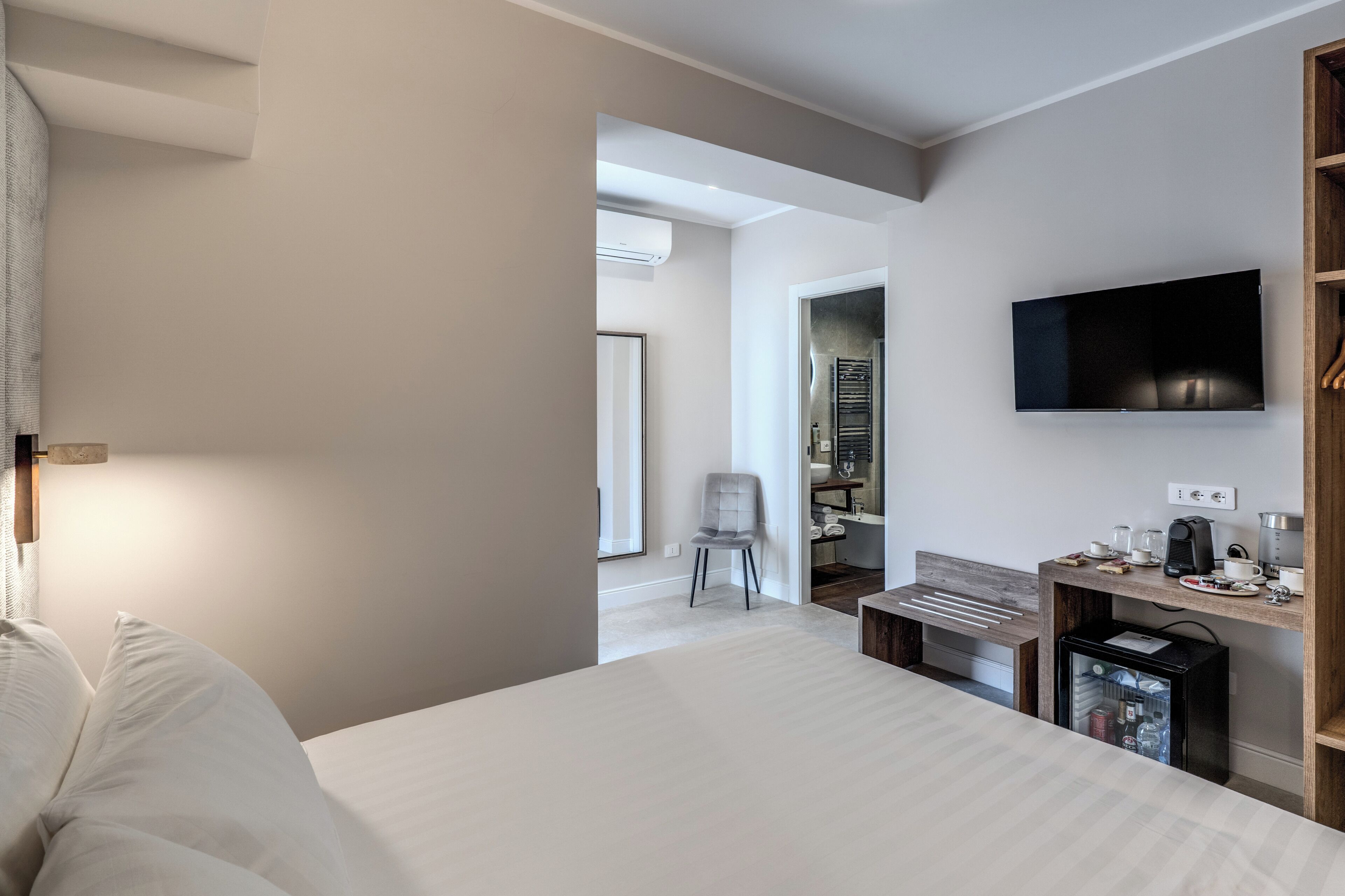 A hotel room with a bed, a desk with a computer, a television, and a small refrigerator.