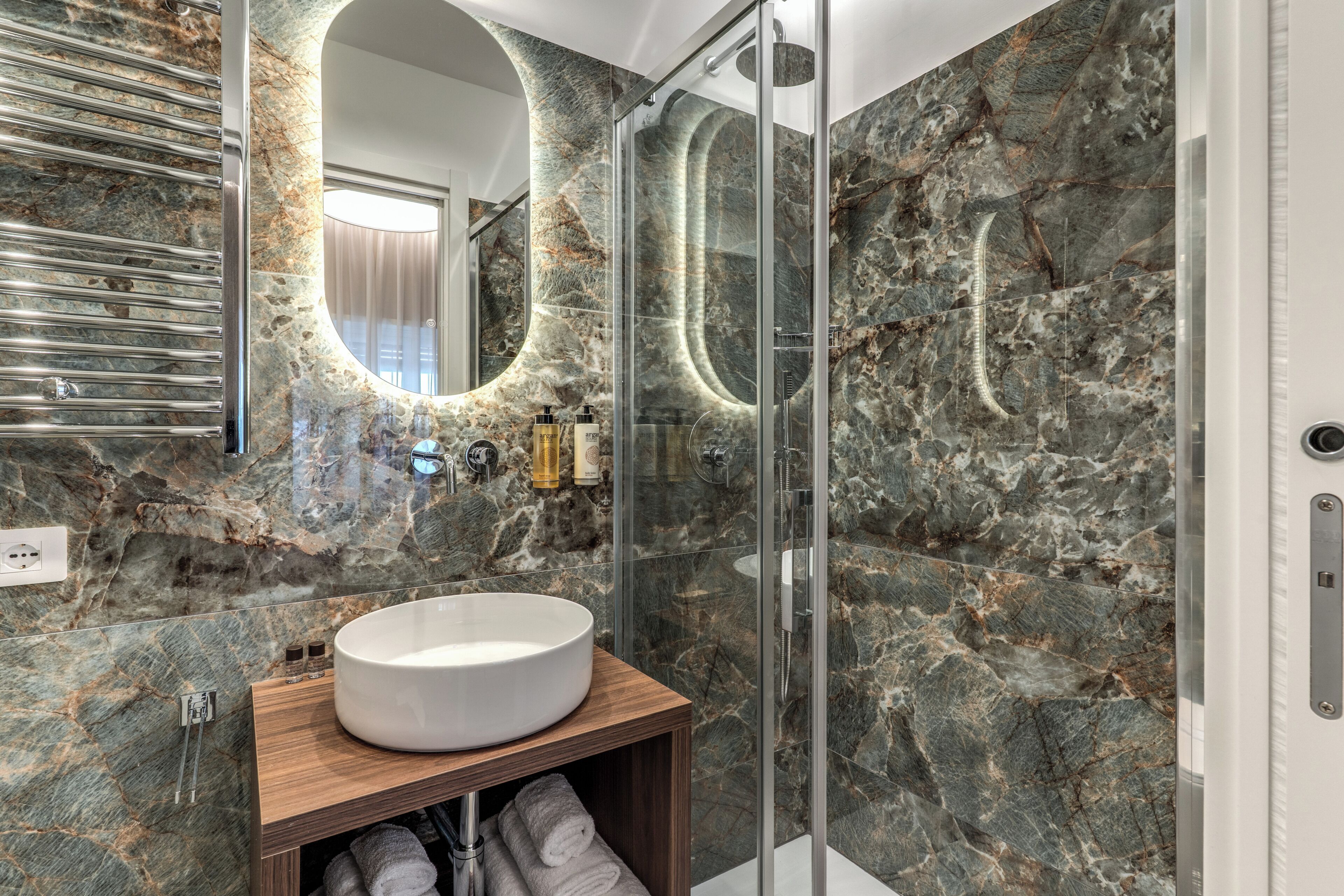 A modern bathroom with a marble wall, a round sink, and a glass shower enclosure.